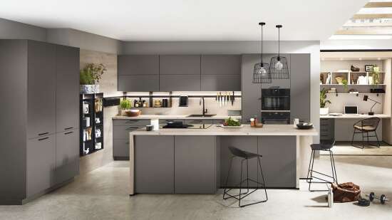Stilvolle Küche mit grauen Schränken, einer Kücheninsel, offenen Regalen, Hängelampen und einem integrierten Arbeitsbereich im Hintergrund.